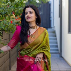 Może przedstawiać: Kobieta w zielono-różowej jedwabnej sari z ozdobnymi złotymi lamówkami. Sari ma tradycyjny indyjski wzór i jest drapowane na ciele w tradycyjny sposób. Kobieta nosi złotą naszyjnik i kolczyki.