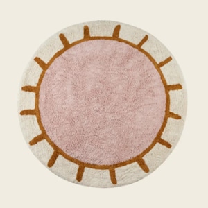May include: A round pink and white rug with a sun design. The sun has a brown outline and white rays.