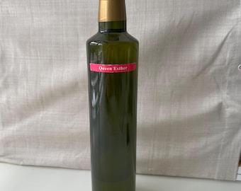 May include: A glass bottle of Queen Esther olive oil with a gold cap. The bottle is filled with a clear, golden liquid.