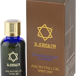 May include: A small glass bottle with a blue cap and a gold label. The label features a gold star of David and the text "The New Jerusalem" and "Anointing Oil" in English and Hebrew. The bottle is sitting on a brown box with a gold star of David and the text "Frankincense & Myrrh" and "Anointing Oil" in English and Hebrew.
