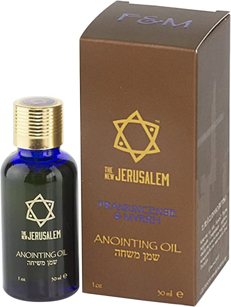May include: A small glass bottle with a blue cap and a gold label. The label features a gold star of David and the text "The New Jerusalem" and "Anointing Oil" in English and Hebrew. The bottle is sitting on a brown box with a gold star of David and the text "Frankincense & Myrrh" and "Anointing Oil" in English and Hebrew.