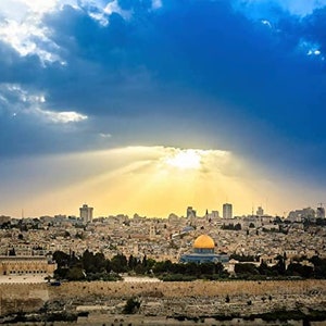 May include: A panoramic view of Jerusalem, Israel, with the Dome of the Rock in the foreground. The city is bathed in golden sunlight, with clouds casting shadows across the cityscape.