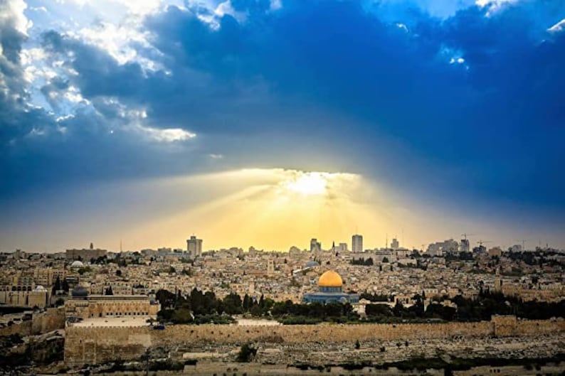May include: A panoramic view of Jerusalem, Israel, with the Dome of the Rock in the foreground. The city is bathed in golden sunlight, with clouds casting shadows across the cityscape.