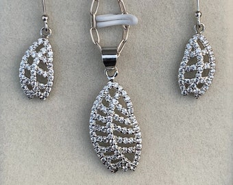 May include: A silver necklace and earrings set featuring a leaf design with clear cubic zirconia stones.