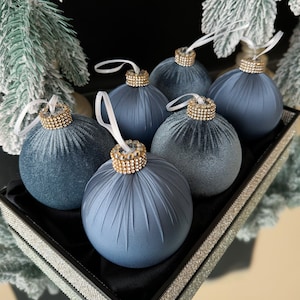 May include: Six blue velvet Christmas baubles with gold and rhinestone accents. The baubles are arranged on a black tray with a sparkly border.