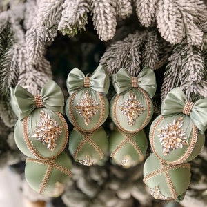 Pode incluir: Cinco enfeites de Natal verde-sálvia com detalhes dourados e pedrarias. Cada enfeite tem um laço de cetim verde-sálvia.
