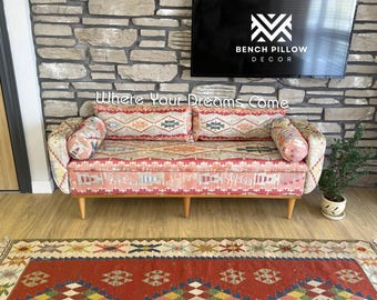 Könnte beinhalten: Ein gemustertes Sofa mit passenden Kissen und Zierkissen. Das Sofa hat Holzbeine und steht vor einer Steinmauer. Der Text "Where Your Dreams Come" ist sichtbar. Ein Teppich befindet sich im Vordergrund.
