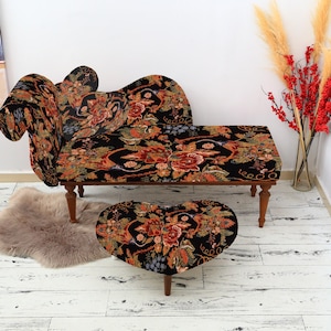 May include: A chaise lounge and heart-shaped ottoman set with a floral pattern in red, orange, and green on a black background. The furniture has wooden legs. A fluffy, light brown rug sits on the floor.