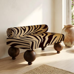 May include: A modern bench with a zebra print fabric in shades of tan and dark brown. The bench has a curved back and is supported by four spherical, dark wood legs. The design is a blend of contemporary and natural elements.
