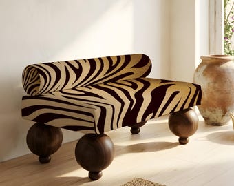 May include: A modern bench with a zebra print fabric in shades of tan and dark brown. The bench has a curved back and is supported by four spherical, dark wood legs. The design is a blend of contemporary and natural elements.