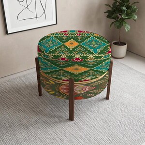 May include: A round ottoman featuring a vibrant green fabric with a multi-colored geometric and floral pattern. The piece is supported by four dark brown wooden legs, providing a stable base for the upholstered seat which displays intricate designs.