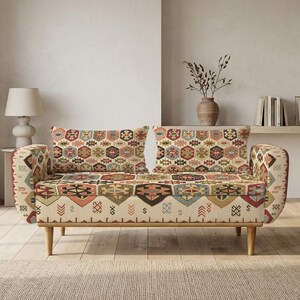 Może przedstawiać: Dwuosobowa sofa z jasnobeżową tkaniną bazową, ozdobioną wielokolorowym geometrycznym wzorem sześciokątów i motywami inspirowanymi stylem plemiennym w odcieniach czerwieni, błękitu, zieleni i brązu, wsparta na czterech nogach z jasnego drewna.