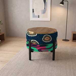 May include: A round ottoman with a wooden top and a gold metal rim. The upper section features a dark blue fabric with a circular patterned design, while the lower section displays a vibrant, abstract wavy print in shades of green, pink, and black.