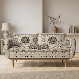 Może przedstawiać: Dwuosobowa sofa z tkaniny w kolorze kremowym z powtarzającym się czarnym wzorem inspirowanym mandalami. Sofa posiada dwie prostokątne poduszki oparciowe, płaskie siedzisko, zaokrąglone podłokietniki oraz cztery jasne, zwężane drewniane nóżki.