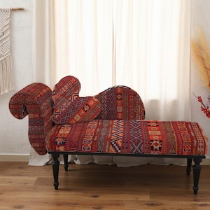 Op de afbeelding: Een rood, patroon chaise longue met zwarte poten. De bekleding heeft een geometrisch ontwerp in rood, oranje en blauw. De chaise longue staat in een kamer met een macramé wandkleed en een kleine bijzettafel. Ongeveer 180 cm lang.