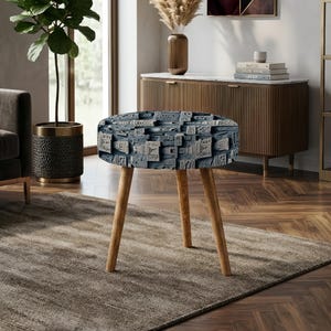 May include: A round side table featuring a textured, dark blue top with a complex, geometric, block-like pattern. The table is supported by three light-colored, tapered wooden legs that extend outward from the center to provide a stable base.
