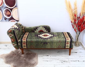 May include: A green and brown patterned chaise longue with wooden legs. The chaise longue is upholstered in a fabric with a geometric design. The chaise longue is sitting on a white wooden floor.