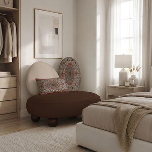 May include: A low-profile, rounded dark brown lounge chair with four spherical wooden feet. It features a large, cream-coloured oval backrest and two decorative pillows with intricate red, blue, and white mandala-style patterns.