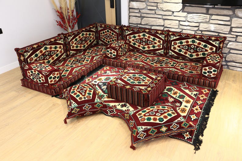 Op de afbeelding: Een modulaire vloerzitting met een rijk patroon. De set bevat hoekbanken, kussens en een kleine poef. De overheersende kleuren zijn bordeauxrood, cr&egrave;me, groen en goud. Ontworpen voor een woonkamer of loungeruimte.