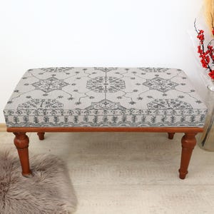 May include: A wooden bench with a grey and black patterned cushion. The bench has four legs and is sitting on a light brown rug.