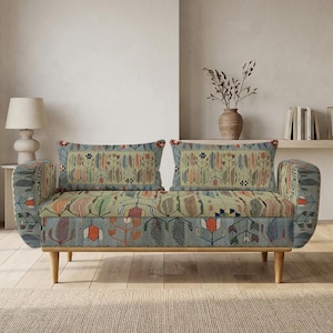 May include: A two-seater sofa featuring a light green fabric upholstery with a multi-colored floral and botanical pattern in shades of orange, blue, and brown. The sofa has two rectangular back cushions, rounded armrests, and four light wood legs.