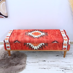 May include: A red and white patterned storage bench with wooden legs. The bench has a geometric design with a central diamond shape.