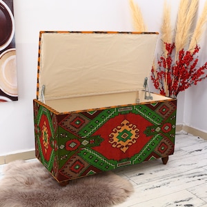 May include: A colorful storage ottoman with a geometric pattern in shades of red, green, and yellow. The ottoman has a hinged lid that opens to reveal a storage compartment.