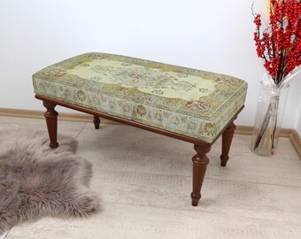 May include: A light green upholstered ottoman with a floral pattern and wooden legs. The ottoman is sitting on a light brown rug.