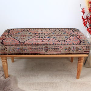 May include: A wooden bench with a colorful patterned cushion. The cushion has a traditional design with shades of pink, blue, and brown.