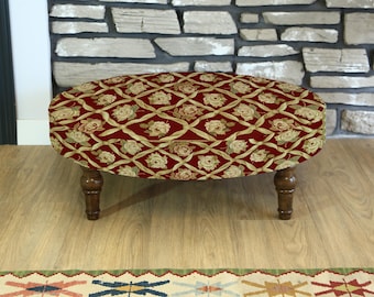 May include: An oval ottoman with a red floral pattern. The fabric features a repeating design of cream-colored roses and ribbons on a deep red background. The ottoman has four dark brown wooden legs.