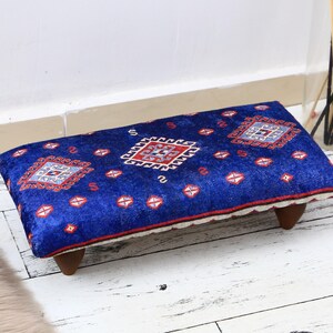 May include: A blue and red patterned footstool with wooden legs. The footstool is made of fabric and has a traditional design.