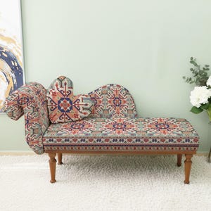 May include: A decorative chaise lounge with a patterned fabric in shades of red, blue, and beige. The wooden frame has four legs. A decorative pillow is on the seat. The chaise lounge is 60 inches long.