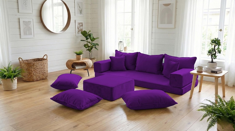 May include: A modular purple sectional sofa with matching throw pillows and an ottoman. The living room setting includes a round mirror, plants, and a woven basket, creating a modern and comfortable space.