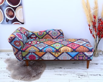 May include: A colourful patterned chaise lounge with a wooden frame and legs. The chaise lounge has a patchwork design with various colours and patterns, including blue, green, red, yellow, and orange.