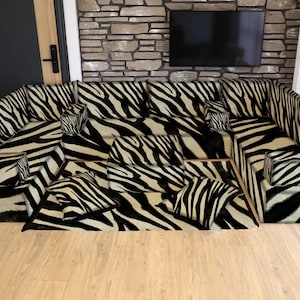 May include: A large sectional sofa with a zebra print pattern. The sofa has a black and white design, with multiple cushions and a matching rug. The furniture is placed in a room with a stone wall and a wooden floor.