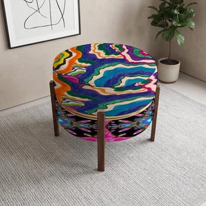 May include: A round ottoman featuring a top cushion with a vibrant, wavy, multi-colored pattern in shades of blue, orange, green, and purple. The base is wrapped in a dark fabric with a colorful, symmetrical graphic print, supported by four legs.