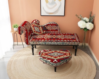 May include: A red chaise lounge and heart-shaped ottoman with a geometric pattern in red, beige, and green. The furniture sits on a beige jute rug. The room has a peach-colored wall and a small side table.