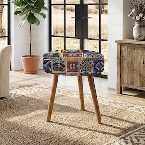 Può includere: Uno sgabello rotondo caratterizzato da un vivace motivo patchwork multicolore con intricati disegni di piastrelle nelle tonalità del blu, giallo, arancione e bianco. Lo sgabello è sostenuto da tre gambe coniche in legno chiaro inclinate.