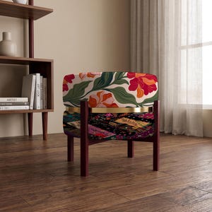 May include: A round stool with a dark wood frame and a gold metal band separating two upholstered sections. The top section features a floral pattern with red, orange, and green leaves on a cream background, while the bottom has a dark floral print.