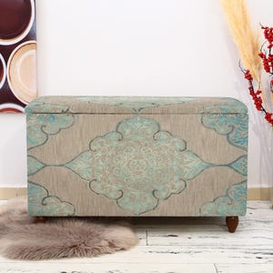 Peut inclure: Un ottoman de rangement décoratif avec un tissu à motifs bleu sarcelle et beige. L'ottoman a une forme rectangulaire et des pieds en bois.