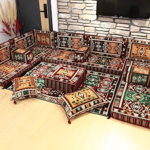 May include: A large, modular floor seating set with a traditional, patterned design. The set includes multiple cushioned sections, pillows, and a low table, all in shades of red, green, and gold. The arrangement is suitable for a living room or lounge area.