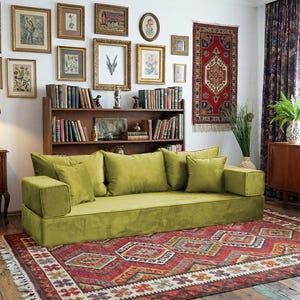 May include: A living room with a green sofa, a patterned rug, and a collection of framed artwork. A Tiffany-style lamp sits on a wooden side table. The room has a vintage, bohemian aesthetic.