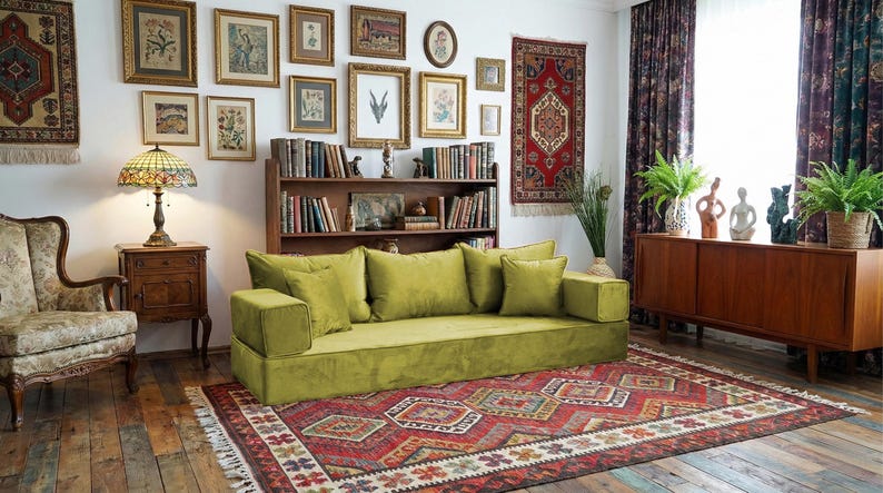May include: A living room with a green sofa, a patterned rug, and a collection of framed artwork. A Tiffany-style lamp sits on a wooden side table. The room has a vintage, bohemian aesthetic.