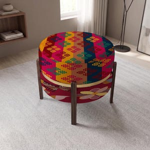 May include: A round ottoman featuring a vibrant, multi-colored geometric pattern on the top cushion and a deep red fabric base with a stylized floral print. The piece is supported by four dark brown wooden legs arranged in a circular frame.