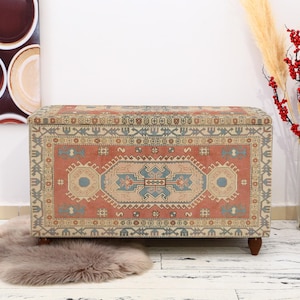 May include: A decorative storage chest with a colorful rug pattern. The chest is made of wood and has a rectangular shape. The chest is sitting on a white floor.