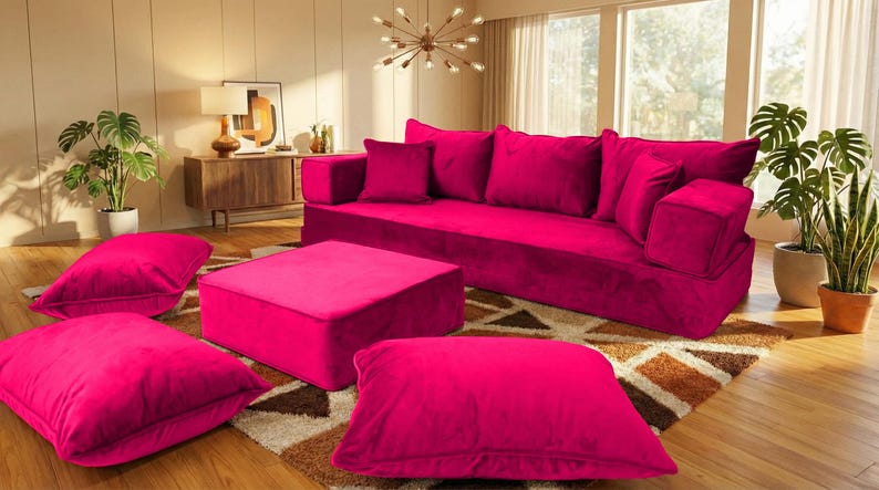 May include: A magenta velvet sofa with matching throw pillows and an ottoman. Several large floor cushions are scattered around the furniture. The room has a rug, plants, and a wooden cabinet.