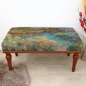 May include: A rectangular ottoman with a landscape painting on the top. The painting depicts a body of water with green and yellow foliage. The ottoman has four brown, turned legs.