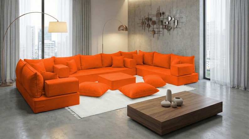 May include: An orange sectional sofa with matching square ottomans and throw pillows. The modern living room also features a wooden coffee table, a white rug, and a floor lamp. The room has large windows with sheer curtains.