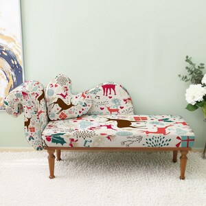 May include: A small chaise lounge with a festive holiday pattern featuring reindeer, gifts, and snowflakes. The fabric is cream-colored with red, green, and brown accents. The wooden legs are a dark brown color. The chaise lounge is approximately 50 inches long.