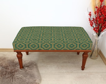 May include: A green and gold patterned bench with wooden legs. The bench is sitting on a light brown rug.